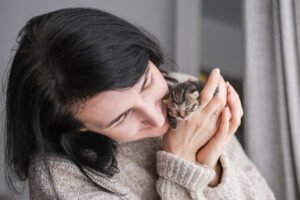 A young woman tenderly hugs a small newborn kitten